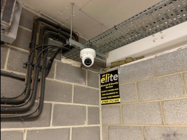 A dome CCTV camera fitted to the ceiling of an underground car park, with its cables run neatly in conduit