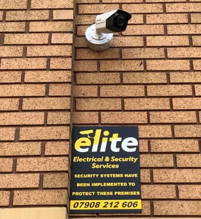 A bullet CCTV camera mounted on a brick wall above an Elite security sign