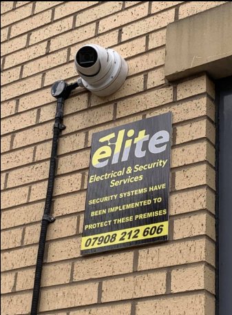 A dome camera on a brick wall above an Elite sign saying security systems protect the premises